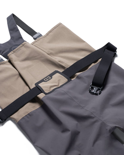 Simms G3Z Pro Stockingfoot Wader - Close-up of a pair of waders in a two-tone color scheme of beige and dark gray, featuring black adjustable straps with plastic buckles and a small G3 logo patch.